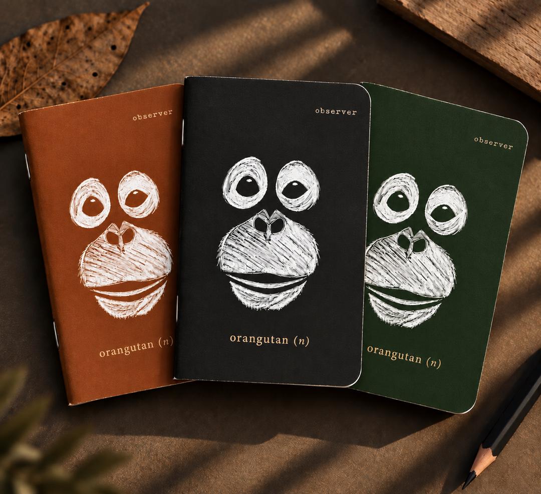 Three Orangutan Pocket Books in brown, black, and forest green covers on a table